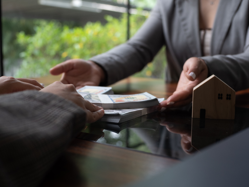 Close-up of hands exchanging money with a small house model