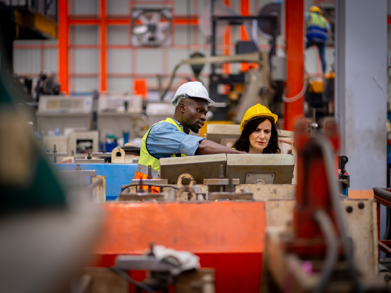 Factory workers in safety helmets examining industrial equipment